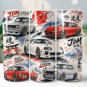 Op de afbeelding: Een cilindervormige roestvrijstalen beker met een rondom lopende afbeelding van Japanse sportwagens, waaronder een witte Supra en rode en zilveren coupés. Het ontwerp bevat kersenbloesems, de berg Fuji, een torii-poort en tekst zoals JDM.