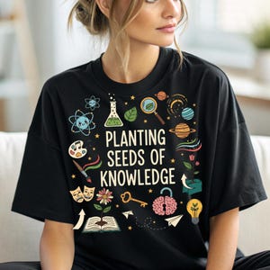May include: Black t-shirt with the phrase "Planting Seeds of Knowledge" in white. The design includes science and art-related illustrations, such as a beaker, planets, a magnifying glass, and a paintbrush. The shirt has a crew neck and short sleeves.