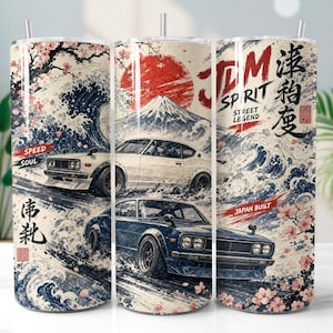 May include: A cylindrical tumbler featuring a graphic print of two vintage sports cars, a large red sun, Mount Fuji, and stylised ocean waves. The design includes cherry blossoms and text that reads JDM SPIRIT STREET LEGEND JAPAN BUILT.