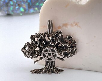 May include: A silver pendant in the shape of a tree with a pentagram in the center. The tree is detailed with intricate branches and a textured trunk.