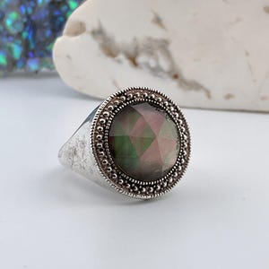 Peut inclure: Une bague en argent avec une grande pierre précieuse irisée à facettes multiples sertie dans une bélière perlée.