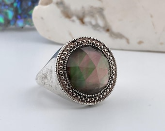 May include: A silver ring with a large, iridescent, multi-faceted gemstone set in a beaded bezel.