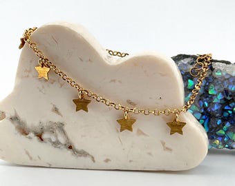 May include: A gold chain bracelet with small star charms hanging from it. The bracelet is on a white marble surface.