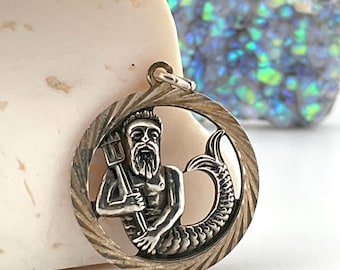 May include: Silver pendant featuring a detailed depiction of the astrological sign Aquarius, a mythical creature with a human torso and a fish tail, holding a trident.