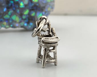 May include: A silver charm in the shape of a high chair. The charm is detailed and has a loop for attaching to a bracelet or necklace.