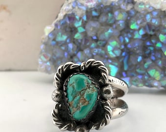 May include: A silver ring featuring a central teardrop-shaped turquoise stone with brown matrix veining. The stone is set in a twisted rope border with small silver spheres at the top and bottom. The band is split into two distinct silver shanks.