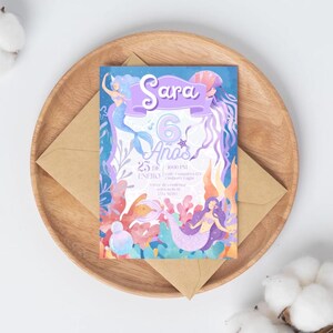 Puede incluir: Una invitación con temática de sirenas con el nombre "Sara" en una pancarta morada. La invitación incluye el texto "6 Años" y otros detalles. El diseño presenta sirenas, corales y medusas en tonos morados, azules y naranjas.