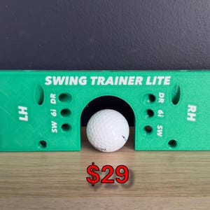 Könnte beinhalten: Ein hellgrünes, rechteckiges Golf-Schwungtrainingsgerät mit einem zentralen Torbogen, in dem ein weißer Golfball liegt. Das Gerät ist mit weißem Text wie SWING TRAINER LITE, LH, RH, SW, 6i und DR sowie mehreren runden Löchern versehen.