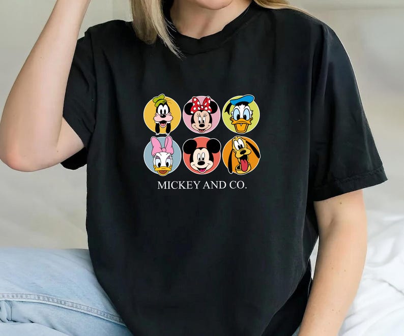 May include: A black short-sleeved t-shirt featuring a graphic print of six Disney characters in circular frames, including Goofy, Minnie Mouse, Donald Duck, Daisy Duck, Mickey Mouse, and Pluto, with the text MICKEY AND CO. printed below.