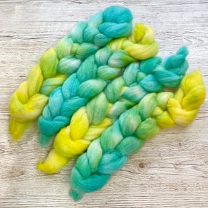 May include: Braided strands of yarn in shades of yellow and blue. The yarn is arranged in a fan shape, with the ends of the strands overlapping.