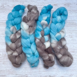 May include: Four strands of hand-dyed yarn in shades of blue, gray, and white. The yarn is braided and ready for knitting or crocheting.