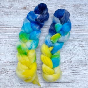 May include: Two braids of hand-dyed wool yarn in shades of blue, green, and yellow. The yarn is braided and ready to be spun into yarn.