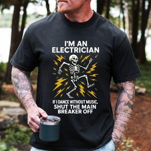 May include: Black t-shirt featuring the text "I'M AN ELECTRICIAN" and a dancing skeleton graphic. The text below the graphic reads "IF I DANCE WITHOUT MUSIC, SHUT THE MAIN BREAKER OFF".
