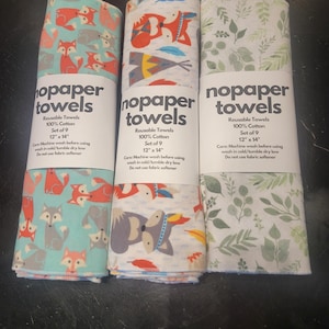 May include: Three sets of reusable paper towels with different designs. Each set is 12 inches by 14 inches and includes 9 towels. The designs include foxes on a teal background, a woodland animal pattern on a white background, and a green leaf pattern on a white background. The text on the labels reads "nopaper towels" and includes care instructions.