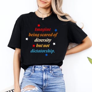 May include: Black t-shirt with a red, white, and blue graphic that says "Imagine being scared of diversity but not dictatorship."