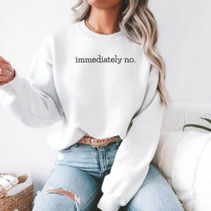 May include: White sweatshirt with the text "immediately no." printed on the front. The sweatshirt is worn by a person wearing blue jeans and a brown belt.