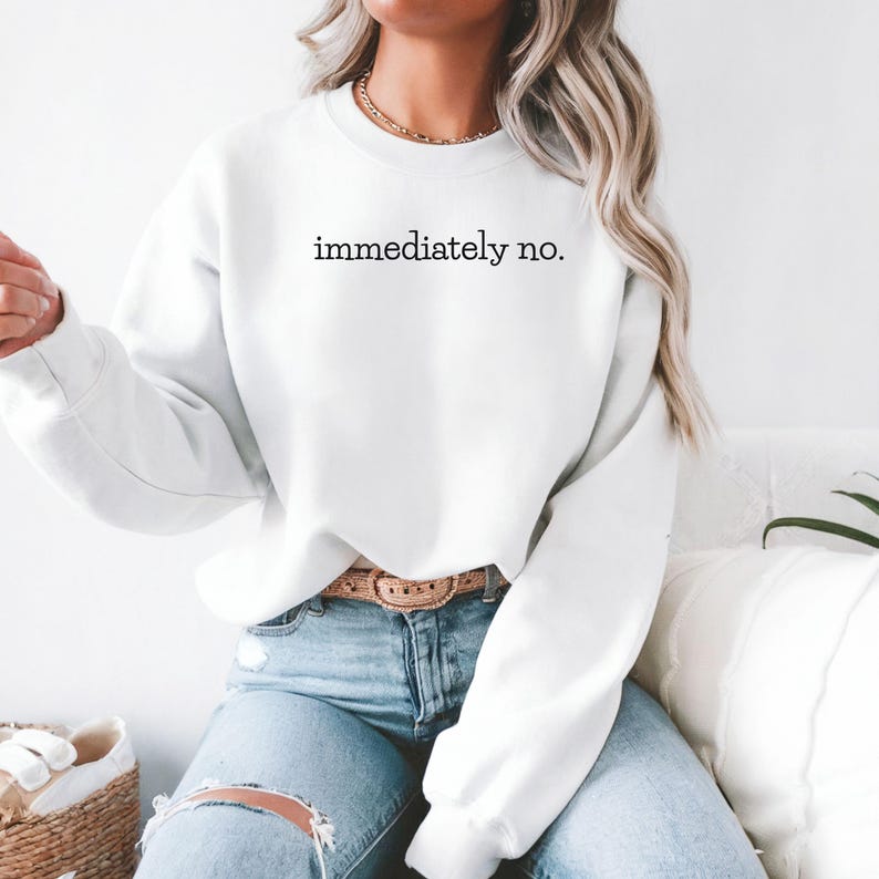May include: White sweatshirt with the text "immediately no." printed on the front. The sweatshirt is worn by a person wearing blue jeans and a brown belt.