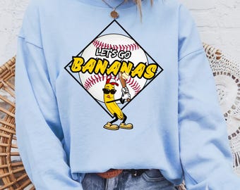 May include: Light blue sweatshirt with a graphic of a banana holding a baseball bat and a baseball with the text "Let's Go Bananas".