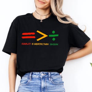 May include: Black t-shirt featuring a graphic of an equals sign, a greater than sign, and a division sign. The text "Equality is greater than division" is printed below the graphic.