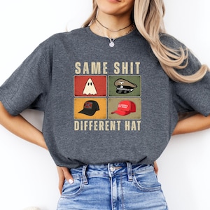 Peut inclure: T-shirt gris foncé avec le texte "SAME SHIT DIFFERENT HAT" et quatre blocs d'images. Les blocs présentent un fantôme, un chapeau militaire, une casquette de baseball noire et une casquette de baseball rouge.