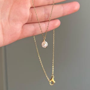 May include: A delicate gold necklace featuring a small, wire-wrapped pearl pendant. The necklace has a fine chain and a lobster clasp. The pearl is white and round, and the gold has a warm, shiny finish. The necklace is displayed against a neutral background.