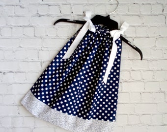 May include: A navy blue sleeveless dress with white polka dots and a white ribbon tie at the shoulders. The dress has a white and gray floral print trim at the hem.