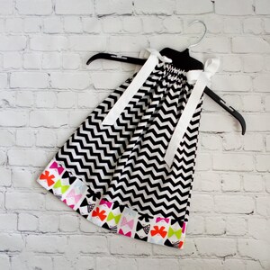 May include: A black and white chevron sleeveless dress with a white ribbon bow at the neckline. The dress has a colorful bow trim around the bottom.