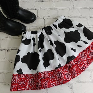 May include: A white and black cow print skirt with a red bandana trim. The skirt has an elastic waistband.