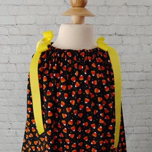 K&ouml;nnte beinhalten: Schwarzes Kleid mit einem Mais-Bonbon-Druck und gelben Schleifenb&auml;ndern.