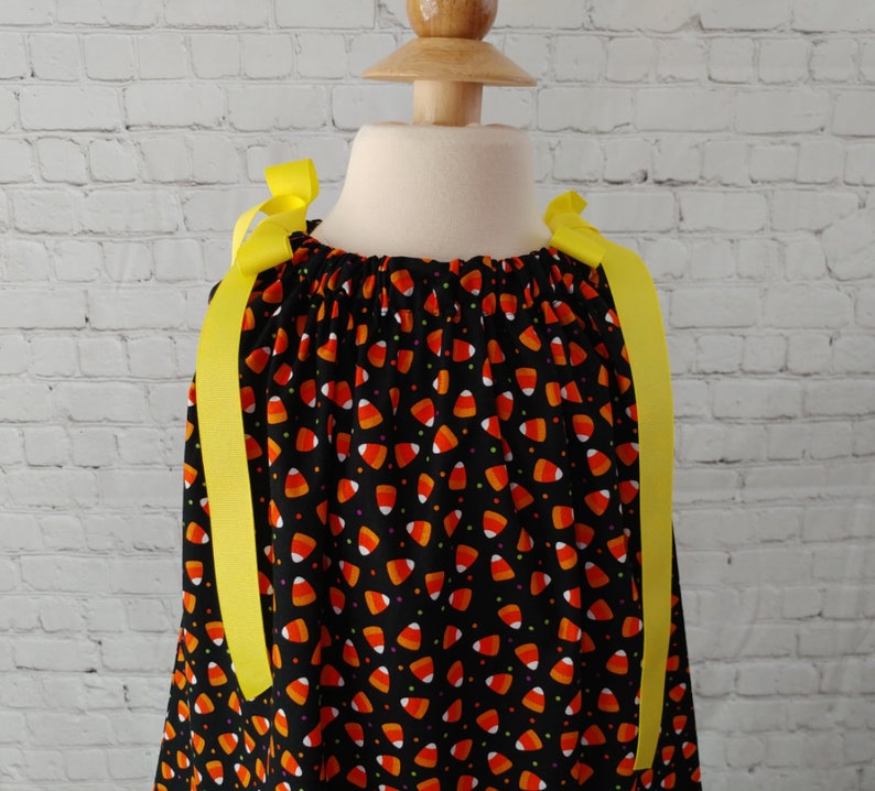 K&ouml;nnte beinhalten: Schwarzes Kleid mit einem Mais-Bonbon-Druck und gelben Schleifenb&auml;ndern.