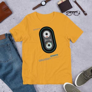 May include: A yellow t-shirt with a graphic of a vintage Sony Walkman cassette player with the text "SONY SPORTS WALKMAN-FM/AM".