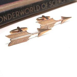 May include: A pair of gold-tone arrow cufflinks. The arrows are detailed with a textured feather design.