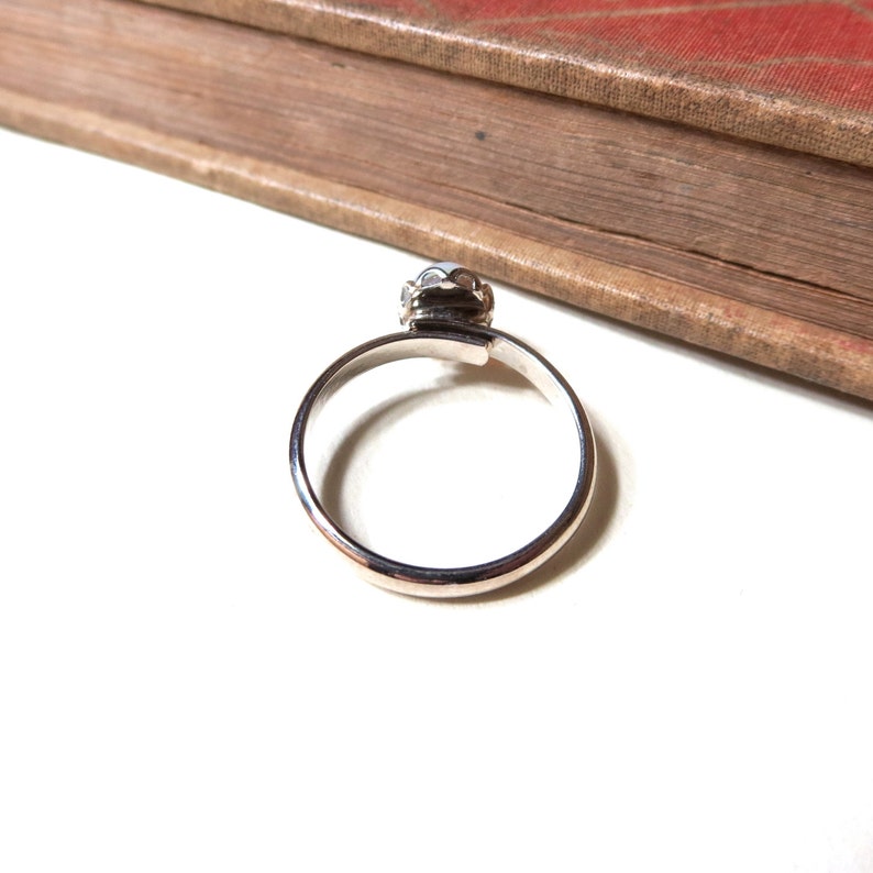 May include: A silver ring with a white stone set in a crown-like design.