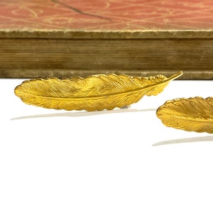 May include: Two gold feather hair clips. The feathers are detailed with a textured design.