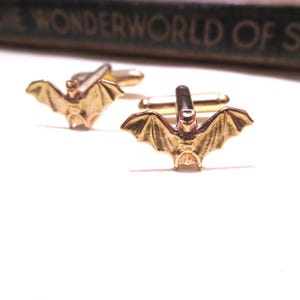 May include: A pair of gold-toned cufflinks featuring a bat design. The bat is detailed with wings and a body.