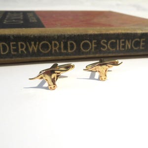 May include: A pair of gold-tone cufflinks featuring a detailed bull head design.