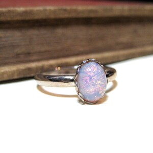 May include: A silver ring with a pale pink opal gemstone set in a delicate, scalloped bezel.