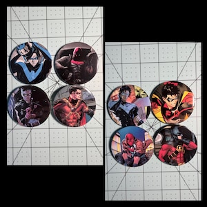 May include: Eight circular pinback buttons featuring various comic book characters in action poses. The designs include figures in blue, red, black, and yellow costumes, with detailed illustrations of heroes in masks and tactical gear on a white grid background.