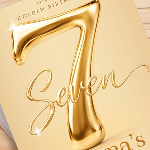 May include: A rectangular card featuring a large, three-dimensional metallic gold number seven. Below the number, the word Seven is written in a flowing, elegant script font. The text IT'S A GOLDEN BIRTHDAY appears at the top, and a partial name ends in 's'.