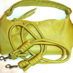 May include: A chartreuse-colored handbag with a matching shoulder strap and an additional detachable strap. The bag has a zippered closure and silver-tone hardware. The straps are knotted for a decorative touch. The bag is made of a shiny, satin-like material.