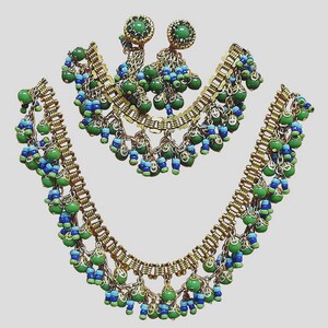 May include: A three-piece jewelry set featuring a necklace, bracelet, and earrings. The set has a gold-tone metal base with dangling green and blue beads. The earrings have a round green stone at the top.