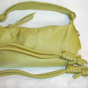 May include: A light green handbag with a matching shoulder strap and a detachable long strap. The bag has a zippered closure and silver-tone hardware. The bag is made of a smooth, shiny material.