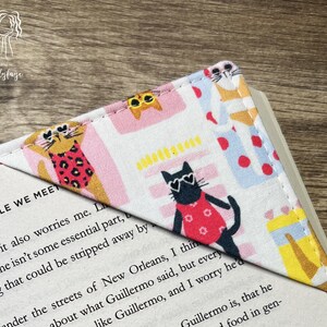 May include: A white fabric bookmark with a pink, yellow, and blue cat pattern. The bookmark is shaped like a triangle and has a stitched edge. The text "PEOPLE WE MEET" is visible on the page.
