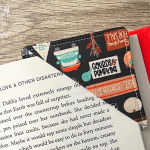 May include: A fabric corner bookmark with a black background featuring pumpkins, gourds, and the text "Gourds & Pumpkins." The bookmark is placed on a book with the title "Love & Other Disasters."