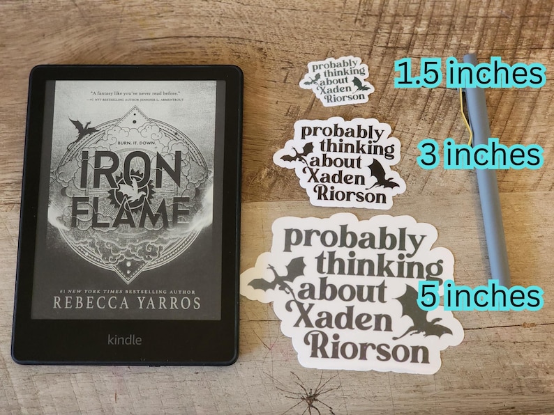 K&ouml;nnte beinhalten: Ein schwarzer E-Reader mit dem Buchtitel Iron Flame, drei wei&szlig;e Aufkleber mit dem Text probably thinking about Xaden Riorson und Drachensilhouetten sowie ein grauer Eingabestift mit Gr&ouml;&szlig;enangaben von 3,8 cm, 7,6 cm und 12,7 cm.