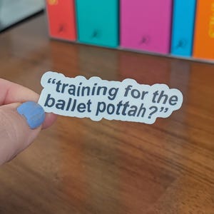 May include: A white die-cut vinyl sticker with a dark blue border and the black text "training for the ballet pottah?" written in a sans-serif font. The sticker has a wavy, irregular shape that follows the contour of the printed text.