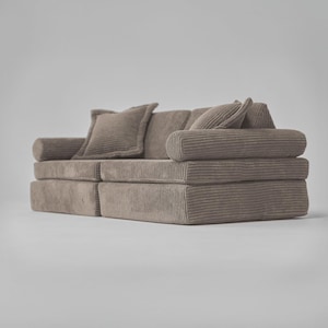 Op de afbeelding: Een bruine corduroy bank met twee kussens. De bank is opgebouwd uit meerdere delen die op verschillende manieren kunnen worden gerangschikt.