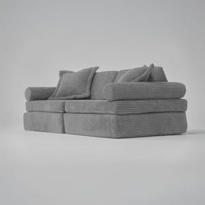 Op de afbeelding: Een grijze corduroy bank met twee kussens. De bank bestaat uit twee aparte delen die aan elkaar kunnen worden bevestigd.