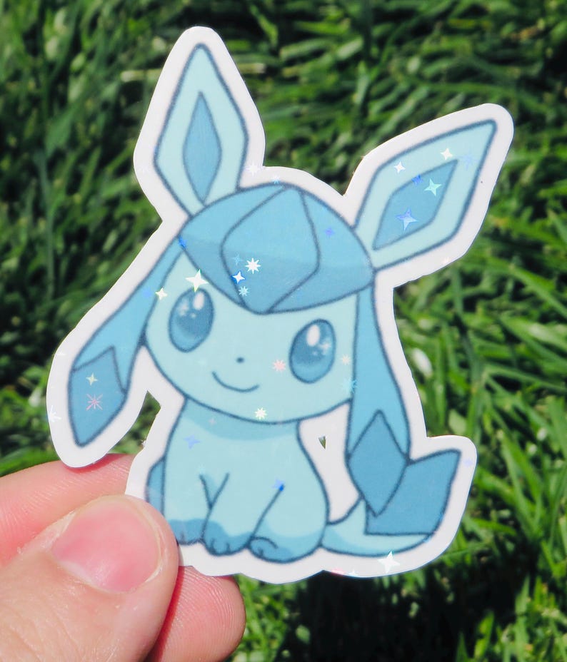 May include: A light blue sticker featuring a cartoon character with large ears and a smiling face. The sticker has a glittery, holographic effect, with star-shaped sparkles. The character is set against a background of green grass.