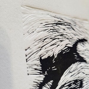K&ouml;nnte beinhalten: Nahaufnahme einer strukturierten, cremefarbenen Oberfl&auml;che mit einem schwarz-wei&szlig;en Grafikdesign. Das Design zeigt ein stilisiertes, abstraktes Bild mit einer Kombination aus schwarzen Vollformen und wei&szlig;en, linearen Details. Das Kunstwerk hat eine handgemachte, k&uuml;nstlerische Ausstrahlung.